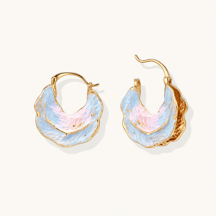 Shell-shaped hoop earrings with iridescent blue-pink enamel and gold trim on cream background