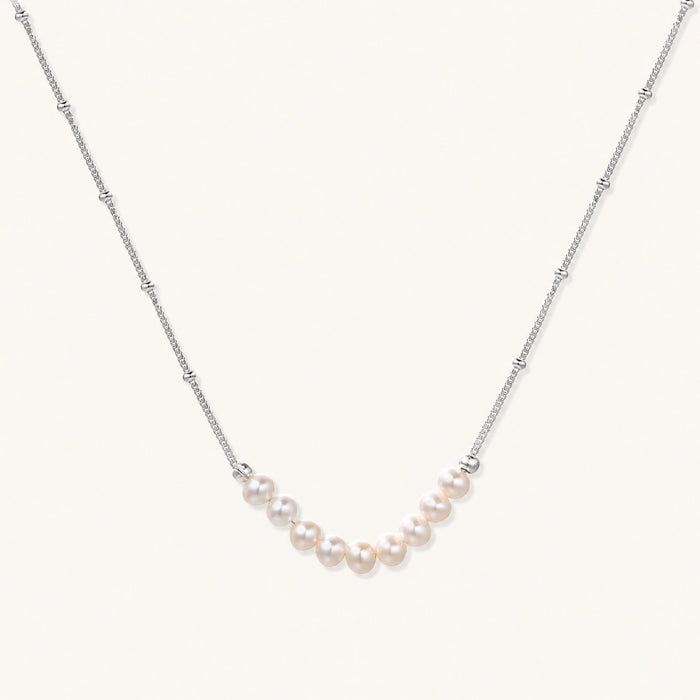 Delicate sterling silver chain necklace with small freshwater pearls arranged in a curved smile arc on cream background.