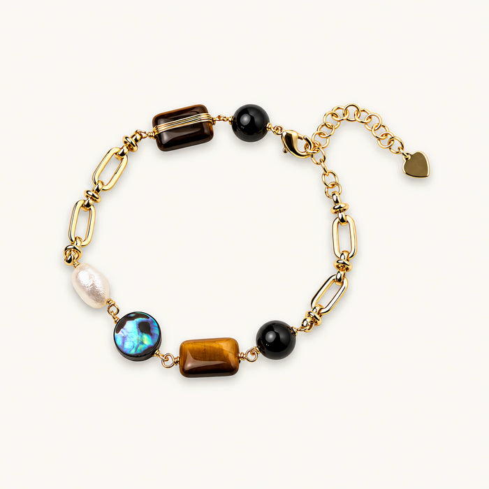 Gold chain bracelet with tiger's eye, obsidian, pearl, and iridescent abalone stones on cream background.