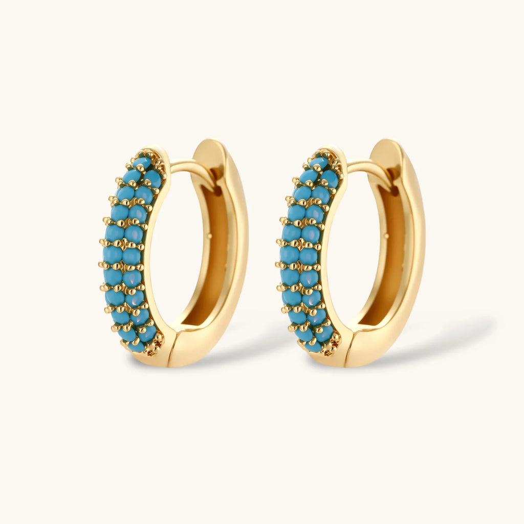 Gold-plated curved necklace and hoop earrings with turquoise cubic zirconia stones on white background.