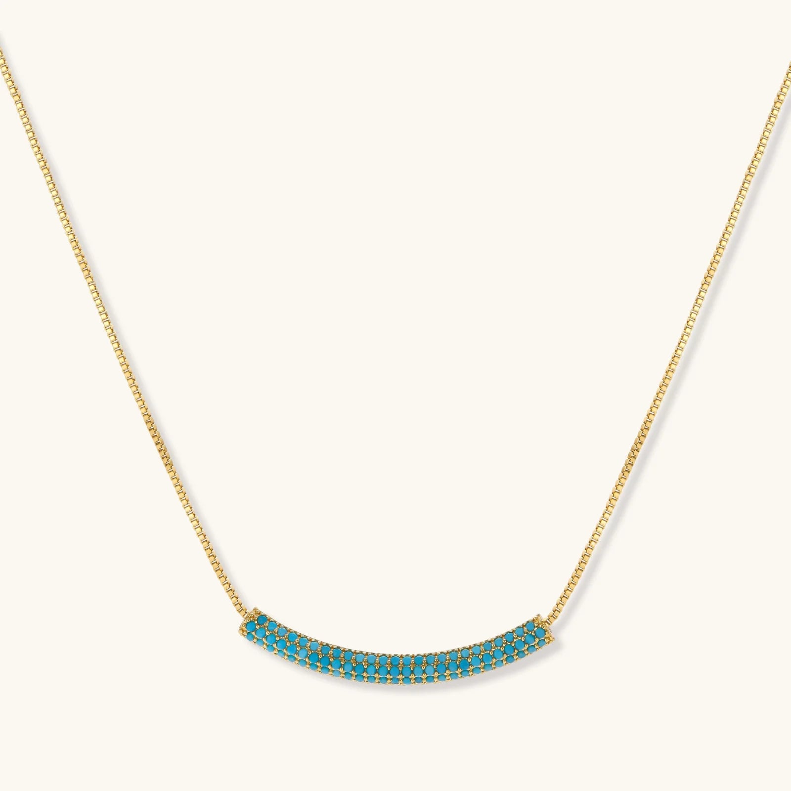 Gold-plated curved necklace and hoop earrings with turquoise cubic zirconia stones on white background.