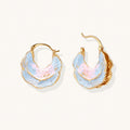 Shell-shaped hoop earrings with iridescent blue-pink enamel and gold trim on cream background