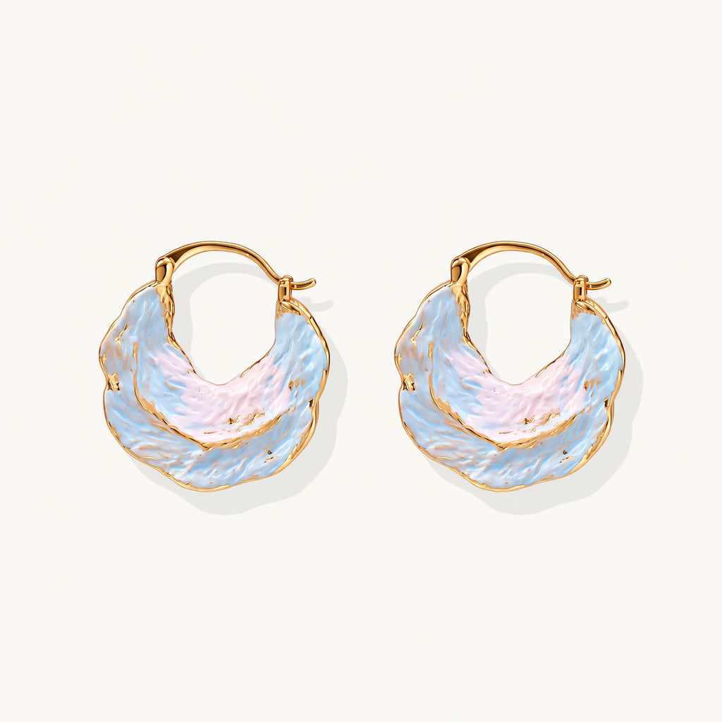 Shell-shaped hoop earrings with iridescent blue-pink enamel and gold trim on cream background