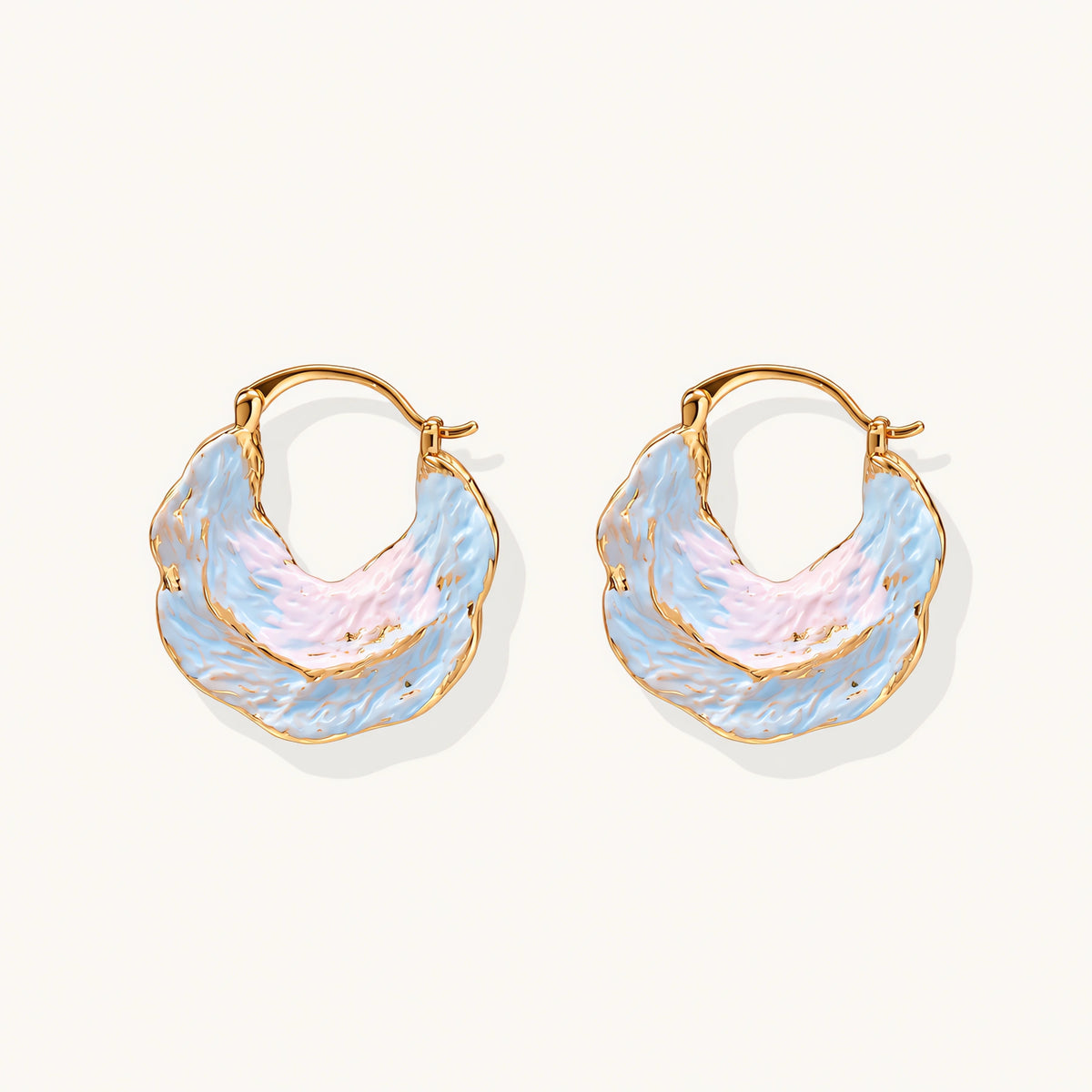 Shell-shaped hoop earrings with iridescent blue-pink enamel and gold trim on cream background