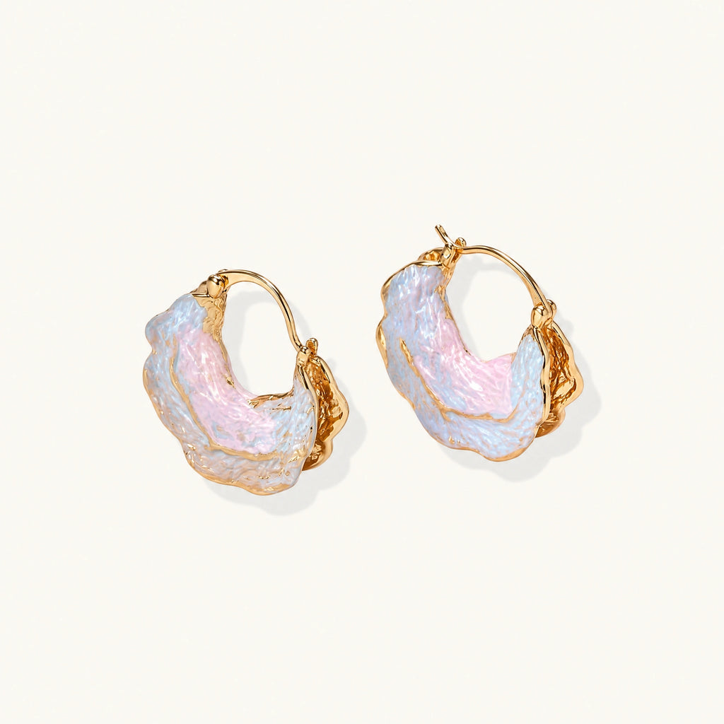 Shell-shaped hoop earrings with iridescent blue-pink enamel and gold trim on cream background