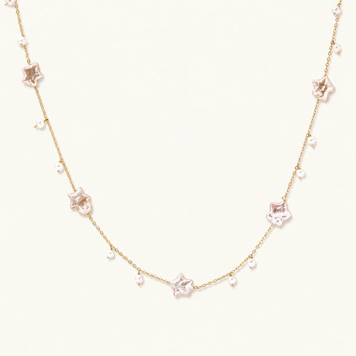 Gold vermeil chain with iridescent star-shaped baroque pearls and small round freshwater pearl drops on cream background.
