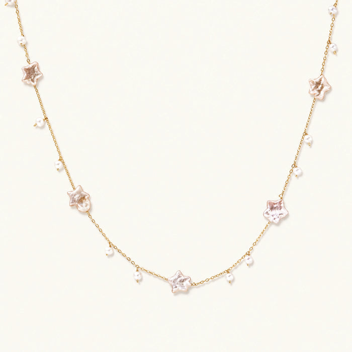 Gold vermeil chain with iridescent star-shaped baroque pearls and small round freshwater pearl drops on cream background.