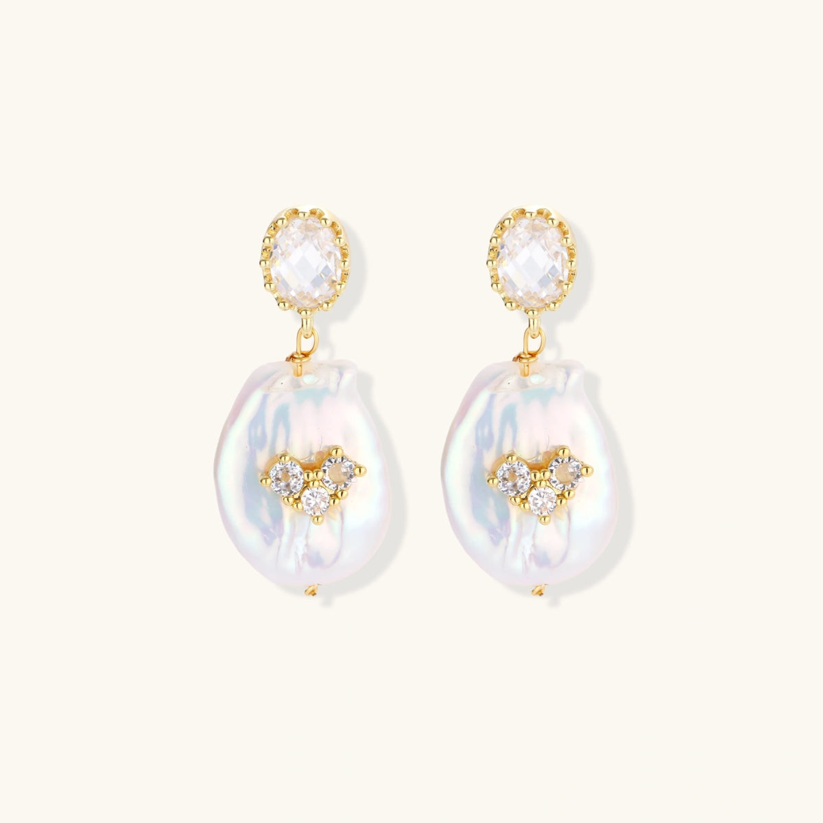 Gold-plated drop earrings with iridescent baroque pearls and crystal flower accents on cream background