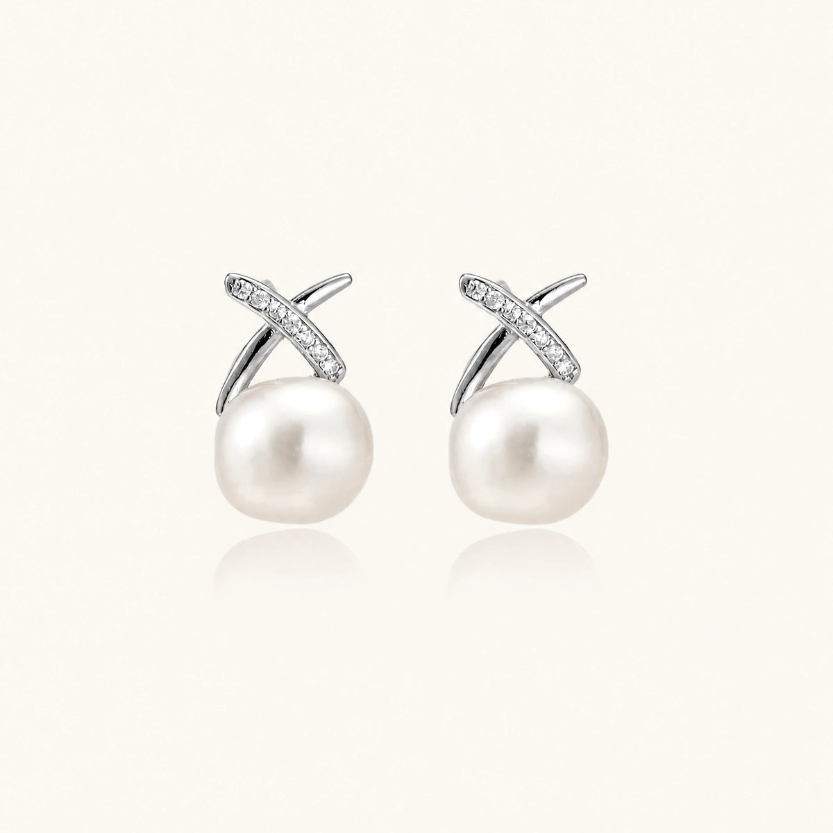 Rhodium-plated silver stud earrings with sparkling X design above lustrous round freshwater pearls on white background.