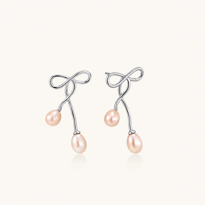 Rhodium-plated silver earrings with organic vine curves and two peachy freshwater pearls on cream background