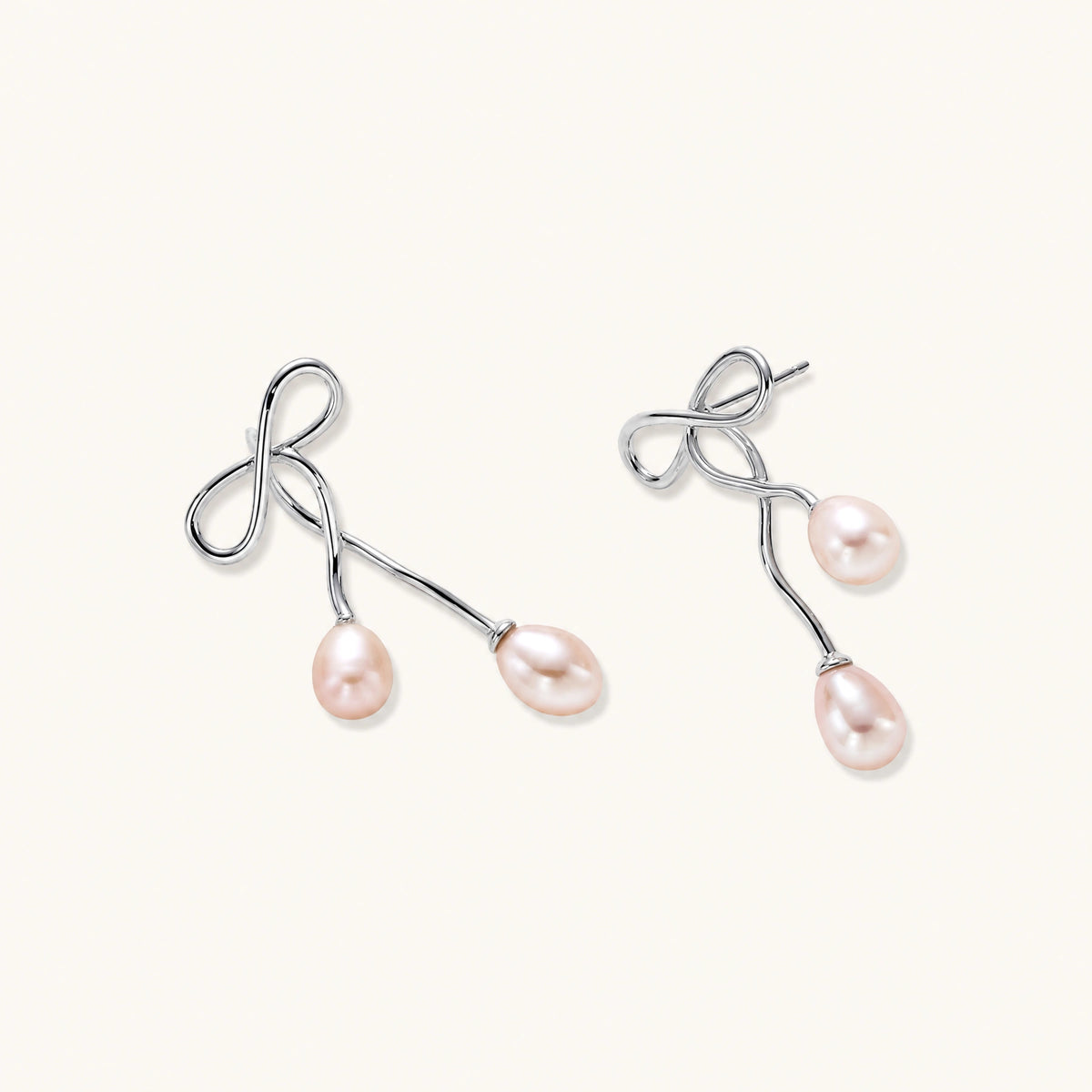 Rhodium-plated silver earrings with organic vine curves and two peachy freshwater pearls on cream background