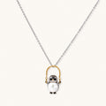 Whimsical penguin pendant holding a white pearl on a gold swing, rhodium-plated silver chain on cream background.