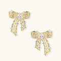 Gold-plated bow earrings with openwork design, marquise center stones, and flowing ribbon tails adorned with zirconia crystals.