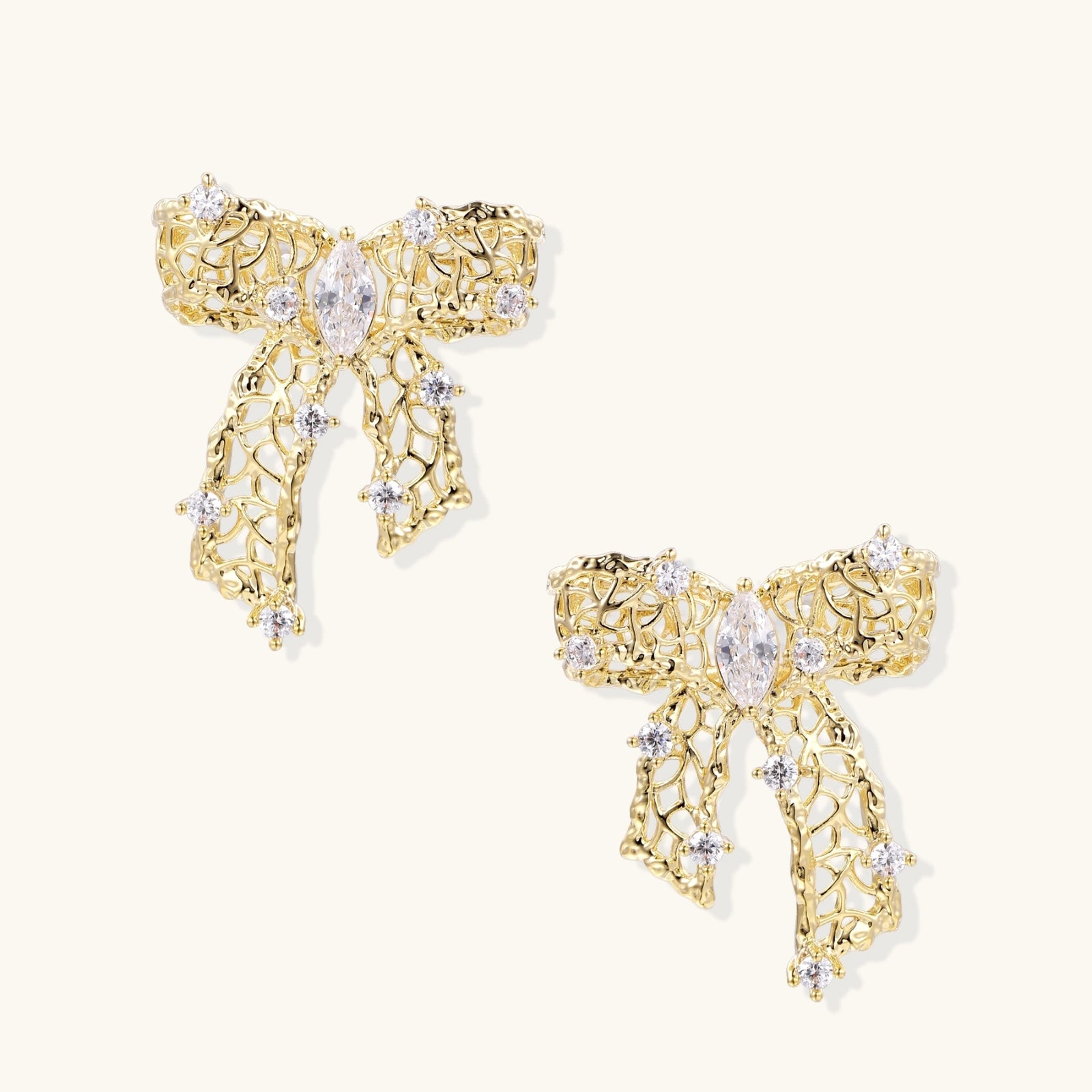 Gold-plated bow earrings with openwork design, marquise center stones, and flowing ribbon tails adorned with zirconia crystals.