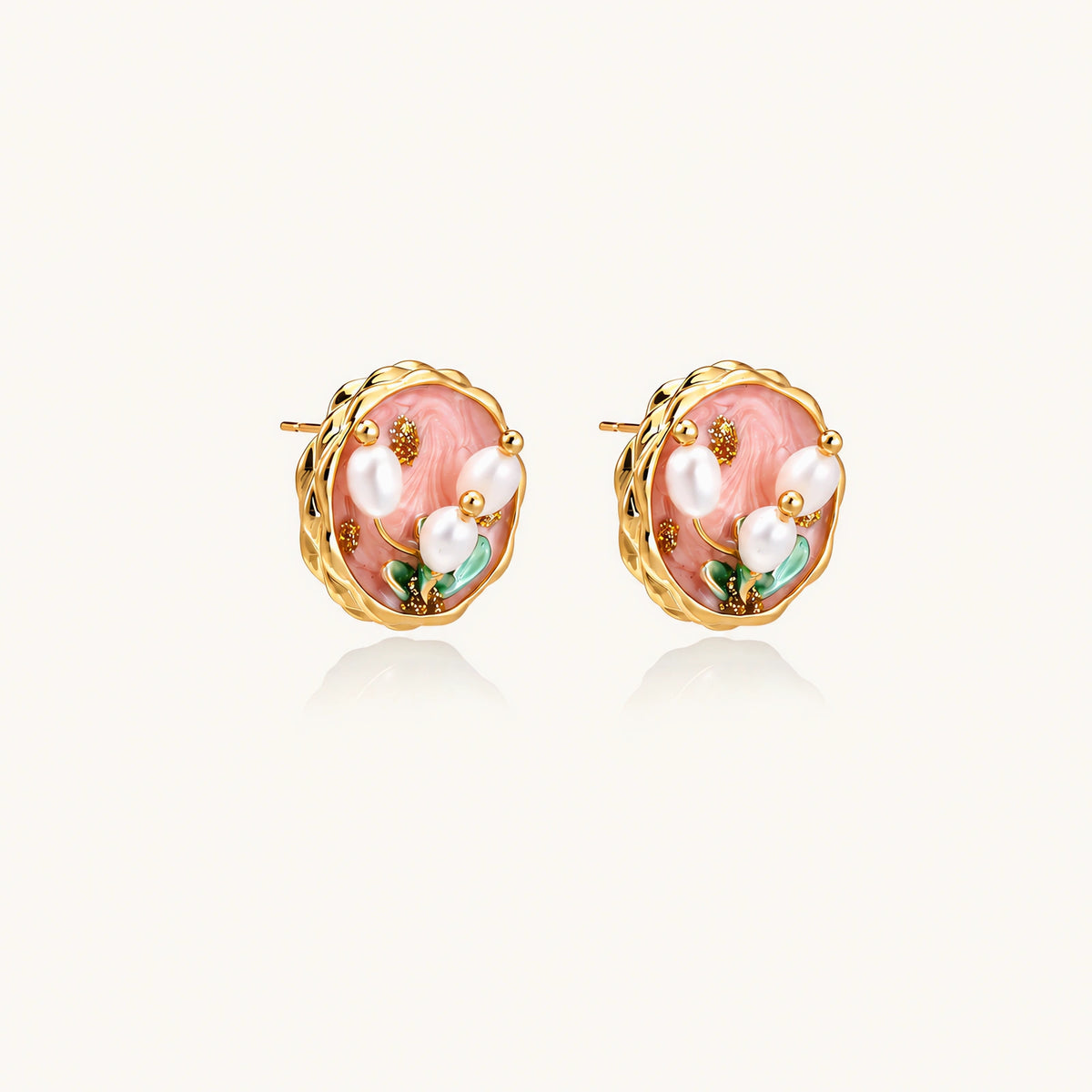 Round stud earrings with pink enamel, three white freshwater pearls, green leaves, and gold-plated braided border