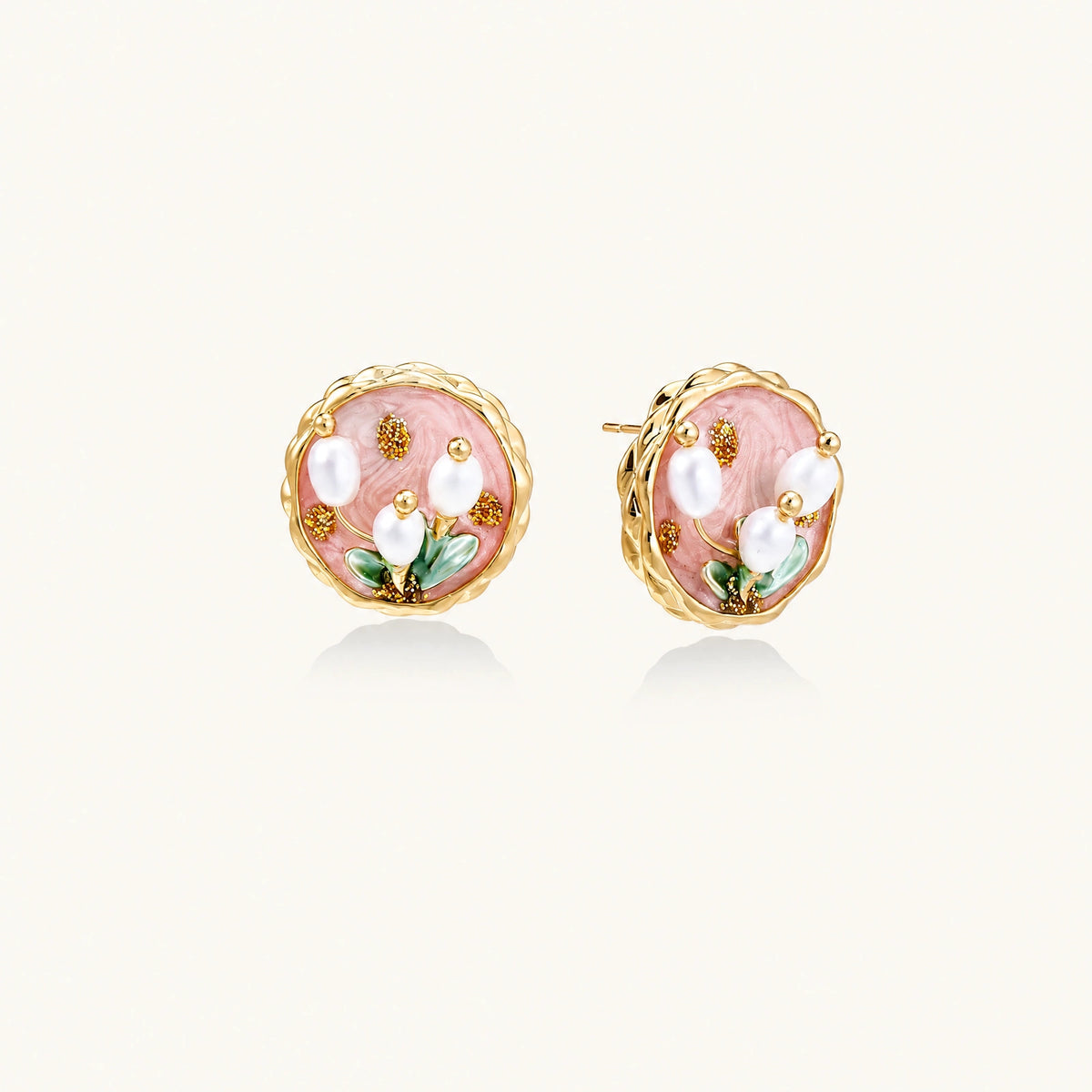 Round stud earrings with pink enamel, three white freshwater pearls, green leaves, and gold-plated braided border