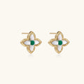 Gold quatrefoil stud earrings with white mother-of-pearl petals and emerald green gemstone center on beige background.