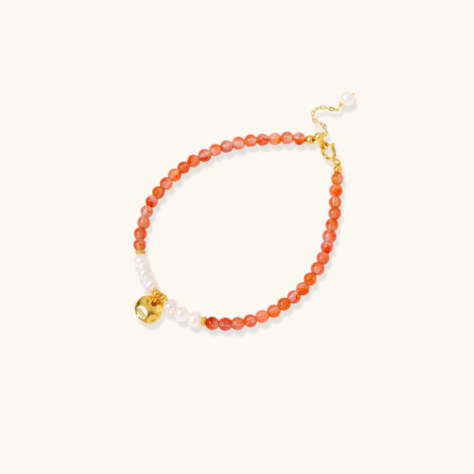 Beaded bracelet with coral-orange carnelian stones, white pearls, and gold heart charm on cream background