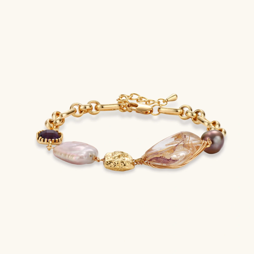 Gold-plated chain bracelet with mixed gemstones including purple stone, baroque pearl, and clear crystal on neutral background.
