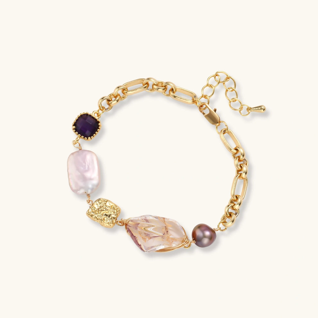Gold-plated chain bracelet with mixed gemstones including purple stone, baroque pearl, and clear crystal on neutral background.
