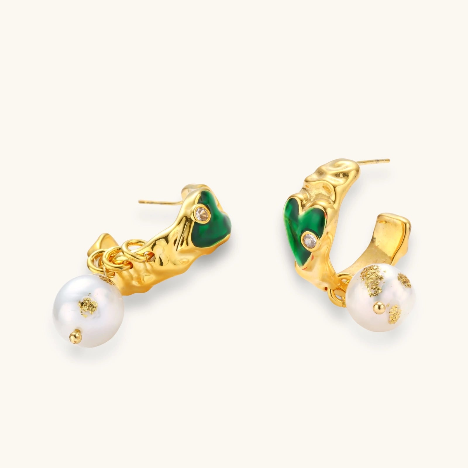 Gold-plated drop earrings with green heart charms and baroque freshwater pearls on neutral background.