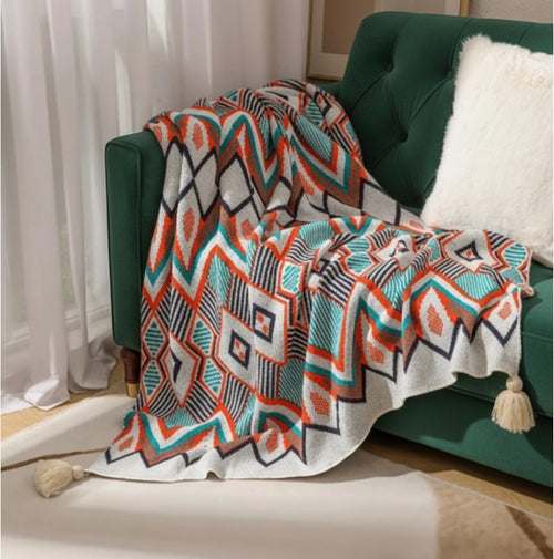 Koc Maison Valentyne w stylu boho z geometrycznym wzorem, ozdobiony frędzlami, narzucony na zieloną sofę.
