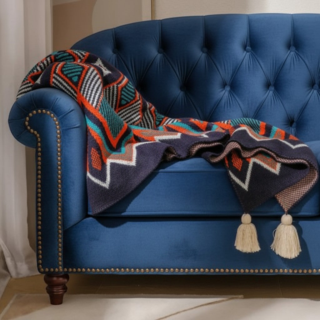 Koc Maison Valentyne w stylu boho z geometrycznym wzorem, frędzlami i akrylowym wykończeniem na niebieskiej sofie.
